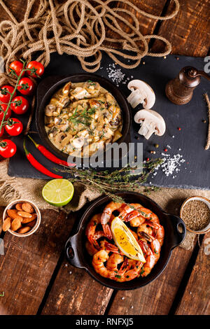 Gran fritto di gamberi in salsa di pomodoro con olio di oliva,funghi in salsa di panna julienne, champignon, prodotti per la cottura sul tavolo di legno sfondo Foto Stock