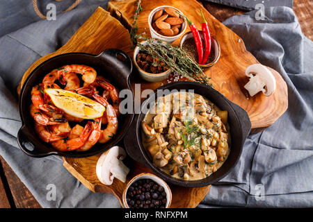 Gran fritto di gamberi in salsa di pomodoro con olio di oliva,funghi in salsa di panna julienne, champignon, prodotti per la cottura sul tavolo di legno sfondo Foto Stock