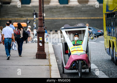 Parigi, Francia - 21 Maggio 2016: l'uomo con la maschera di protezione alla guida della sua rickshaw su Paris street - alto livello di inquinamento atmosferico e cattivo ambiente nel centro di Parigi, con i mezzi di trasporto pubblici Foto Stock