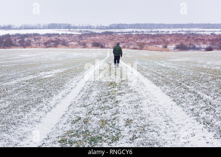 Uomo con cane sulla strada innevata su giovani campo di grano sul tempo di primavera Foto Stock