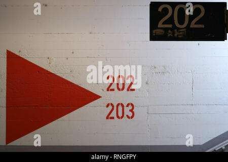 Il dipinto di bianco parete di calcestruzzo alla fine di un tunnel di stazione con dipinti di frecce direzionali e numeri di piattaforma. Foto Stock