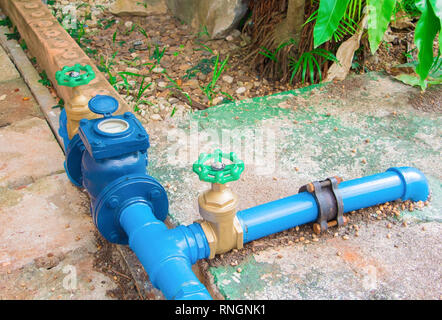 Valvole in ottone di acqua con la manopola verde a giunto di collegamento vecchia tubazione in acciaio blu vernice. sul pavimento di cemento al di fuori degli edifici industriali Foto Stock