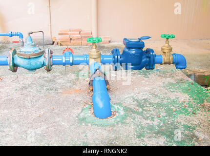 Valvole in ottone di acqua con la manopola verde a giunto di collegamento vecchia tubazione in acciaio blu vernice. sul pavimento di cemento al di fuori degli edifici industriali Foto Stock