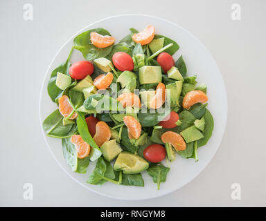 Primo piano della materie frutta fresca e insalata di verdure con spinaci, mandarini arance, uva pomodori e spinaci su una piastra bianca. Foto Stock