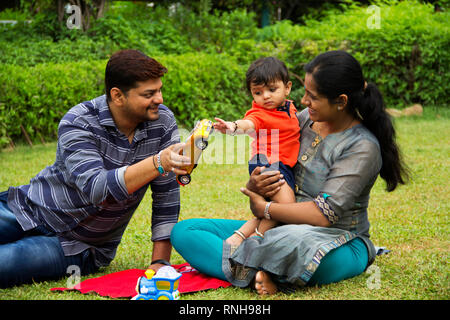 Felice famiglia indiana, padre dando giocattolo auto a suo figlio per bimbi, seduta con sua madre, giardino interno, Pune, Maharashtra Foto Stock