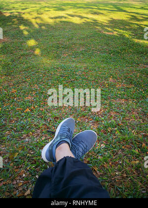 Donna di gambe in scarpe grigio a sedersi su foglie secche nel parco. Foto Stock