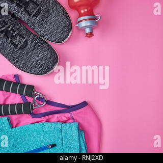 Tessuto nero scarpe e altri elementi per il fitness su uno sfondo rosa, vista dall'alto Foto Stock
