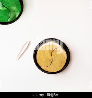 Moderno concetto di cosmetici. Oro e verde occhio viso patch in vaso con le pinzette. Patch di idrogel. Anti invecchiamento e sollevamento . La pelle del viso cura. Idratare Foto Stock