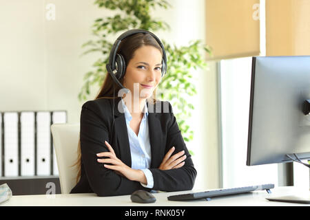 Fiducioso lavoratore di ufficio che indossa la cuffia guarda la fotocamera con bracci ripiegati al lavoro Foto Stock