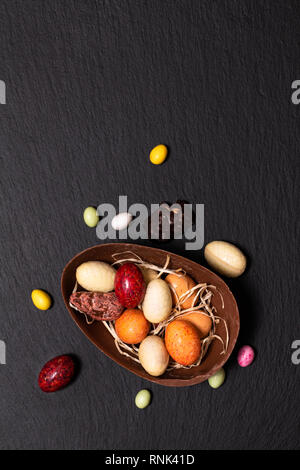 Vacanze concetto alimentare caramelle colorate e uova di pasqua di cioccolato nero sulla piastra di ardesia con spazio di copia Foto Stock