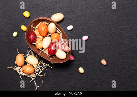 Vacanze concetto alimentare caramelle colorate e uova di pasqua di cioccolato nero sulla piastra di ardesia con spazio di copia Foto Stock
