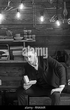 Educazione sostenibile concetto. Ragazzo con stile con capelli e barba la lettura di un libro. Gentleman in vacanza in cottage di legno Foto Stock