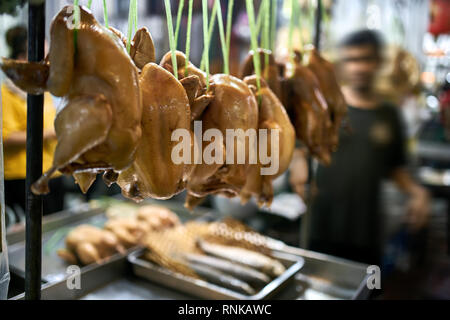 Corpi di pollo sono appesi sulle corde di verde su vassoi di cromo su sfondo sfocato della strada del mercato di Bangkok in Thailandia. Orizzontale. Foto Stock