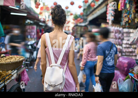 Bruna ragazza in un rosa striato dress passeggiate sull'Asian street market durante la celebrazione del nuovo anno lunare in Bangkok in Thailandia. Ella ha un paglierino Foto Stock