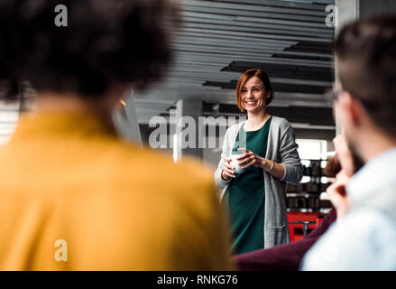 Un gruppo di giovani imprenditori ascoltando una presentazione in ufficio, parlando. Foto Stock