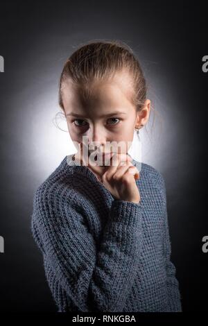 Teen girl 9-12 anni, guarda nel telaio, emotiva ritratto in studio su uno sfondo grigio con retroilluminazione Foto Stock