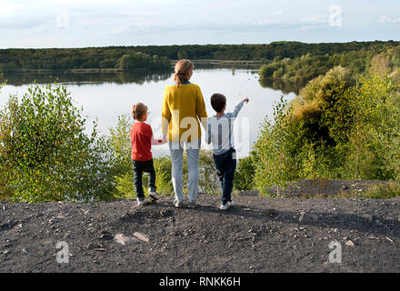 Donna, madre con i suoi due figli, tenendo le mani, rivolta verso il lago ' Lac de la Mare ' in Goriaux, nella foresta di Raismes-Saint Amand Wallers, scarpata Foto Stock