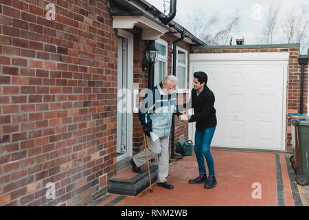 Ragazzo adolescente sta aiutando il suo nonno fuori della porta e scendere le scale di casa sua. Foto Stock