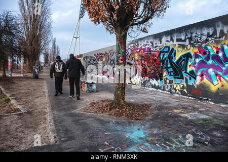 Mauer Park,Berlino, due uomini a piedi lungo i graffiti parete coperta in inverno, deserte parcheggio vuoto al crepuscolo Foto Stock