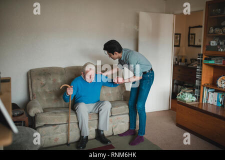 Ragazzo adolescente sta aiutando il nonno di alzarsi dal divano nel salotto di casa sua. Foto Stock