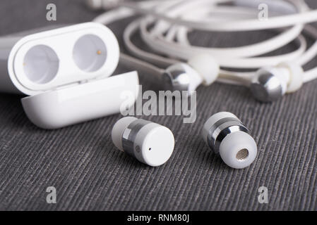 Wireless bluetooth cordless auricolari con custodia caricabile su uno sfondo di cavo auricolare Foto Stock