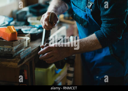 Immagine ravvicinata di un uomo anziano con una pialla surform su legno nella sua bottega. Foto Stock