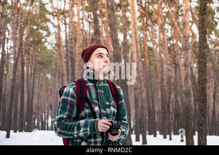 Escursionismo persona di sesso maschile in inverno forest scattare fotografie. Uomo in inverno a scacchi shirt in bellissimi boschi innevati con una vecchia telecamera cinematografica Foto Stock