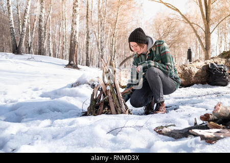 Facendo un falò in un nevoso foresta di betulla. Persona di sesso femminile nei pressi di un incendio su una soleggiata giornata invernale nel bosco Foto Stock