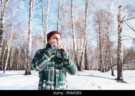 Persona di sesso maschile di bevande da una tazza in un inverno nevoso foresta. Uomo in camicia a scacchi detiene tazza di caffè all'aperto e gode di bel tempo Foto Stock