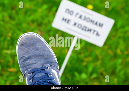 Gli adolescenti piede oltre l'erba verde vicino sfocato striscione bianco con testo russo: non camminare sui prati! Foto Stock
