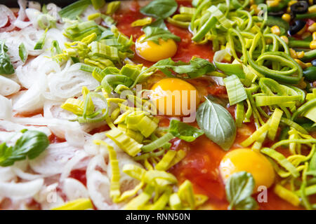Pizza cruda con uova, porro, ketchup, la cipolla, il basilico e altri ingredienti Foto Stock