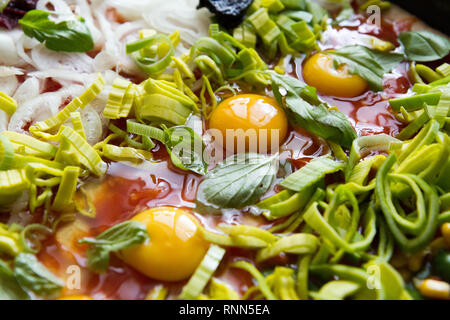 Pizza cruda con uova, porro, ketchup, la cipolla, il basilico e altri ingredienti Foto Stock
