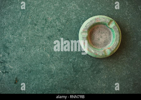 Composizione astratta di un vecchio e polveroso posacenere verde sul tavolo verde. Foto Stock