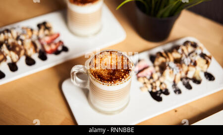 Banner dimensioni di due tazze di latte caldo con cotto crosta di caramello e rotolo dolce con banana e fragola sul tavolo di legno in coffee-shop. Caffè conc Foto Stock