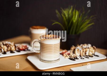 Due tazze di latte caldo con cotto crosta di caramello e rotolo dolce con banana e fragola sul tavolo di legno in coffee-shop. Concetto di caffè. Foto Stock