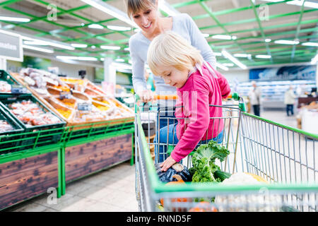Madre avente il suo bambino a cavallo nel carrello del supermercato Foto Stock