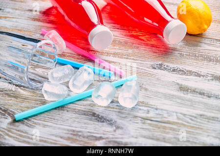 Bottiglie di plastica con frutti di bosco, bevanda rinfrescante. sparsi di cubetti di ghiaccio e bere cannucce. Sullo sfondo di uno squallido tavolo in legno. close up. copia Foto Stock