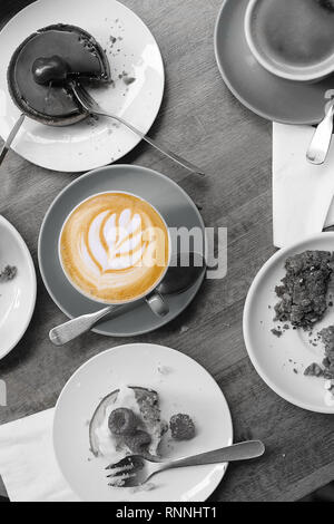 Tavolo da pranzo riempito con metà mangiato del cibo con una tazza piena di caffè incontaminati e decorate con la schiuma di latte art. Foto in bianco e nero e a colori. Foto Stock