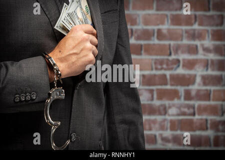 Uomo brasiliano tenendo distinte dei soldi con un manette in un carcere. concetto di corruzione, politici corrotti, affari illegali. Sfondo mattone. Foto Stock