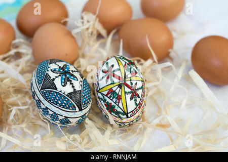 Tradizionale a mano le uova di Pasqua in paglia sul panno bianco e pochi organici di uova fresche in background. Modello tradizionale da Bucovina Foto Stock