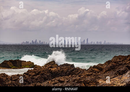 Oceano onde schiacciamento sul Snapper rocce con la Gold Coast skyline della città in background Foto Stock