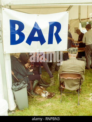 Un anziano uomo seduto in ingresso alla tenda di birra presso il locale agricolo mostra visto da dietro mentre i clienti socalise interno, Highlands scozzesi Foto Stock