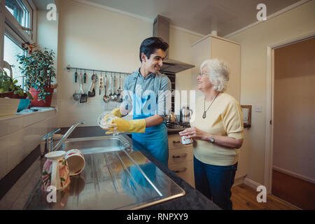 Ragazzo adolescente sta parlando con sua nonna mentre Egli lava i piatti nella sua cucina. Foto Stock