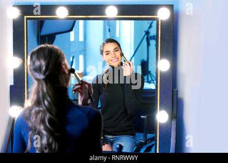 Ritratto di stupendo giovane donna di applicare il suo specchio mentre è seduto in corrispondenza dello specchio nel photostudio. Foto Stock