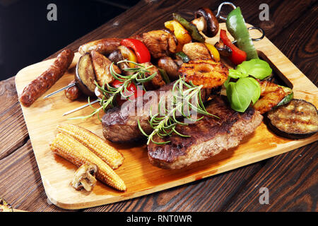 Un assortimento di deliziose grigliate di carne con verdure ed erbe sul tavolo rustico Foto Stock