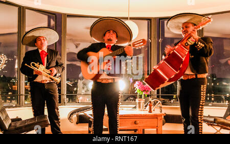 Scena in interni di un trio di mariachi messicani musicisti in costume tradizionale a un party privato, movimento sfocato Foto Stock