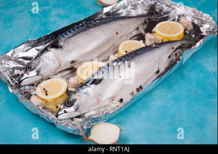 Sgombro pesce con ingredienti per la cottura in un foglio di alluminio su uno sfondo blu. Un foglio di alluminio è un comune prodotto domestico. Foto Stock