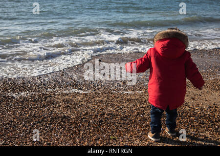 Il Toddler giocando sulla spiaggia di ciottoli di un cappotto invernale Foto Stock