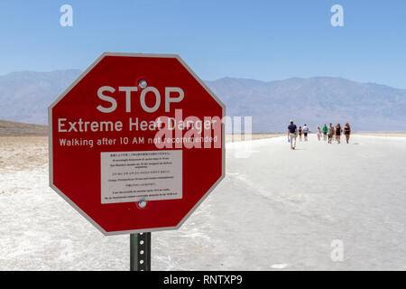 Un 'STOP calore estremo pericolo' firmare visto come la gente inizia a piedi sul bacino Badwater, Parco Nazionale della Valle della Morte, California, Stati Uniti. Foto Stock