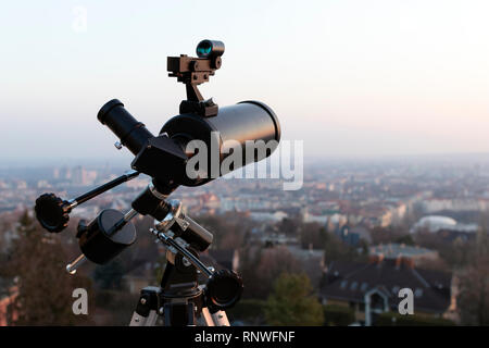 Un professionista di telescopio newtoniano montato su un treppiede, guardando una grande città al tramonto Foto Stock
